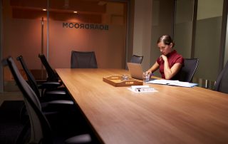 A person with a laptop sitting at a table in a boardroom